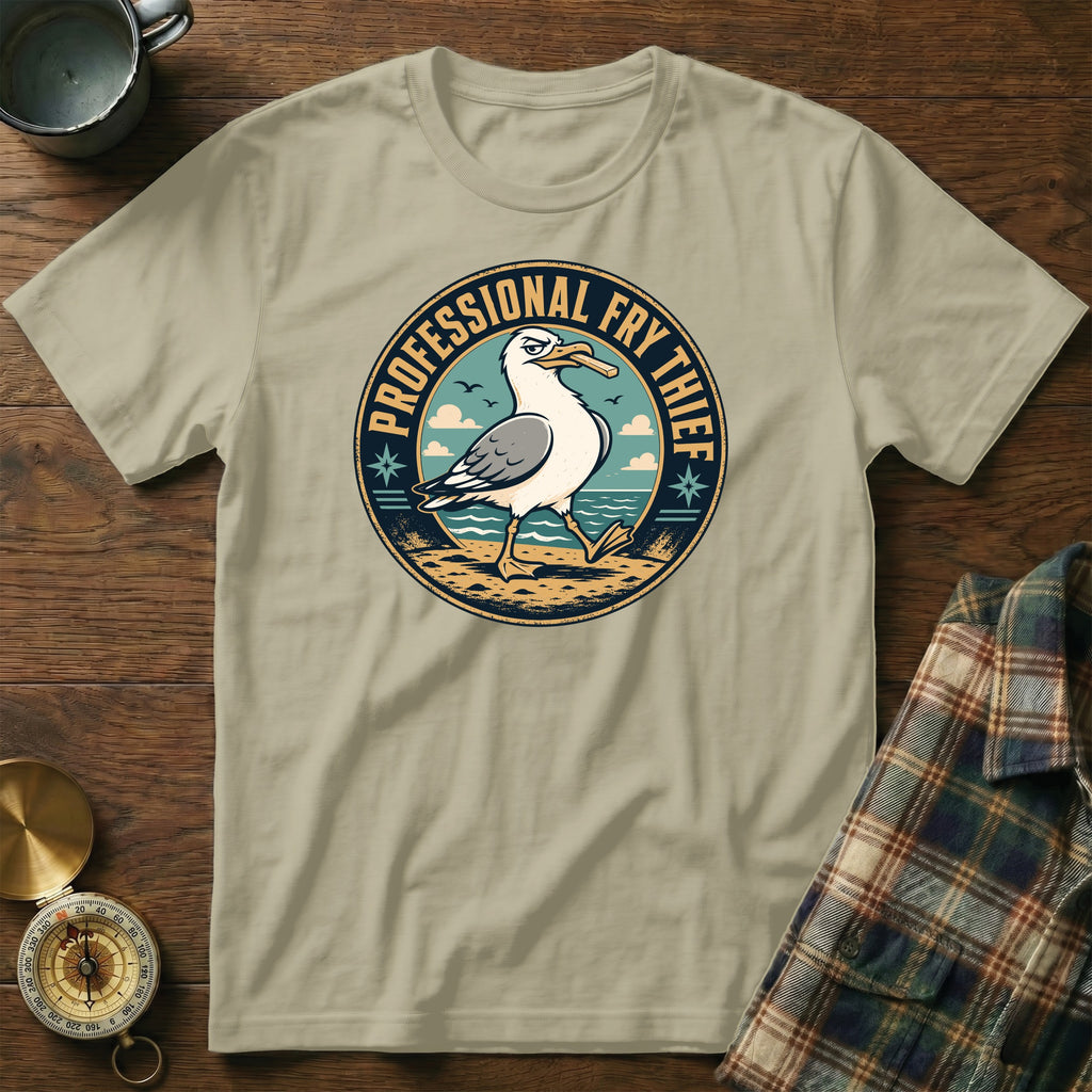 Seagull with a piece of food in its beak on a beach, "PROFESSIONAL FRY THIEF" text.
