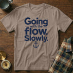 Taupe crewneck t-shirt with navy blue text that reads Going with the flow. Slowly., accented with an anchor illustration.