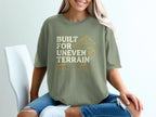 Olive green t-shirt with "Built for Uneven Terrain" text and mountain graphic.