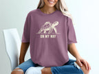 Purple t-shirt with a cream graphic of a turtle wearing a backpack and text "ON MY WAY".