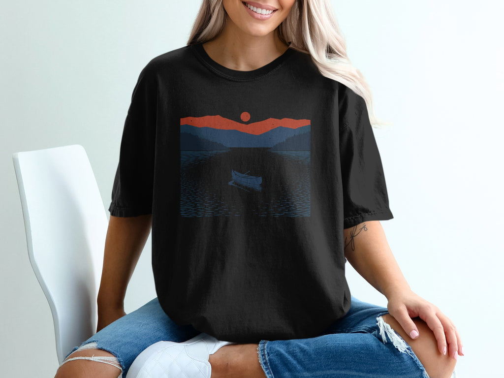 Black t-shirt with a minimalist sunset landscape of mountains and a lone canoe on a lake.