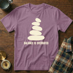 Purple t-shirt with stacked stones graphic and "BALANCE IS OVERRATED" text.