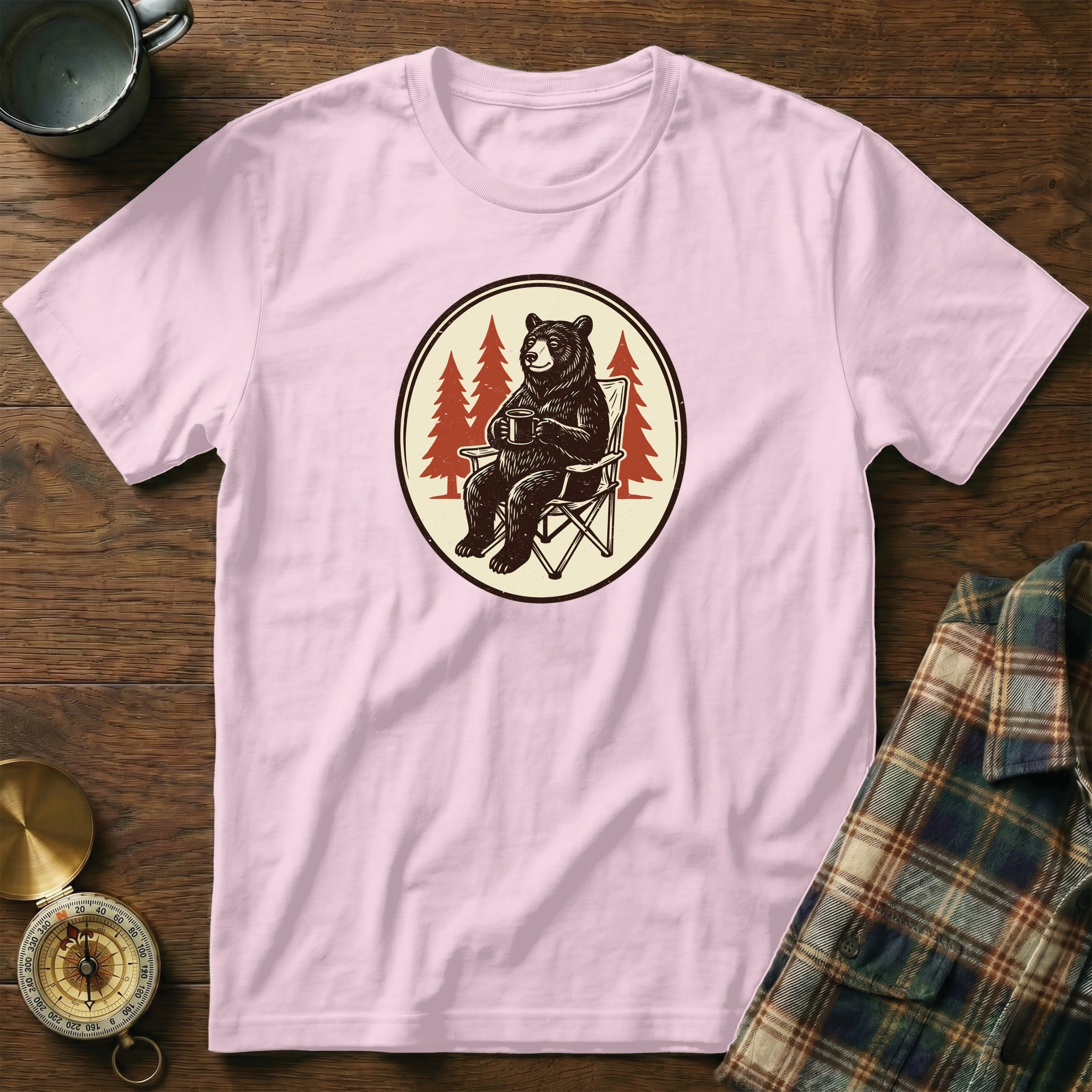 Pink t-shirt featuring a graphic of a bear holding a mug in a camping chair.