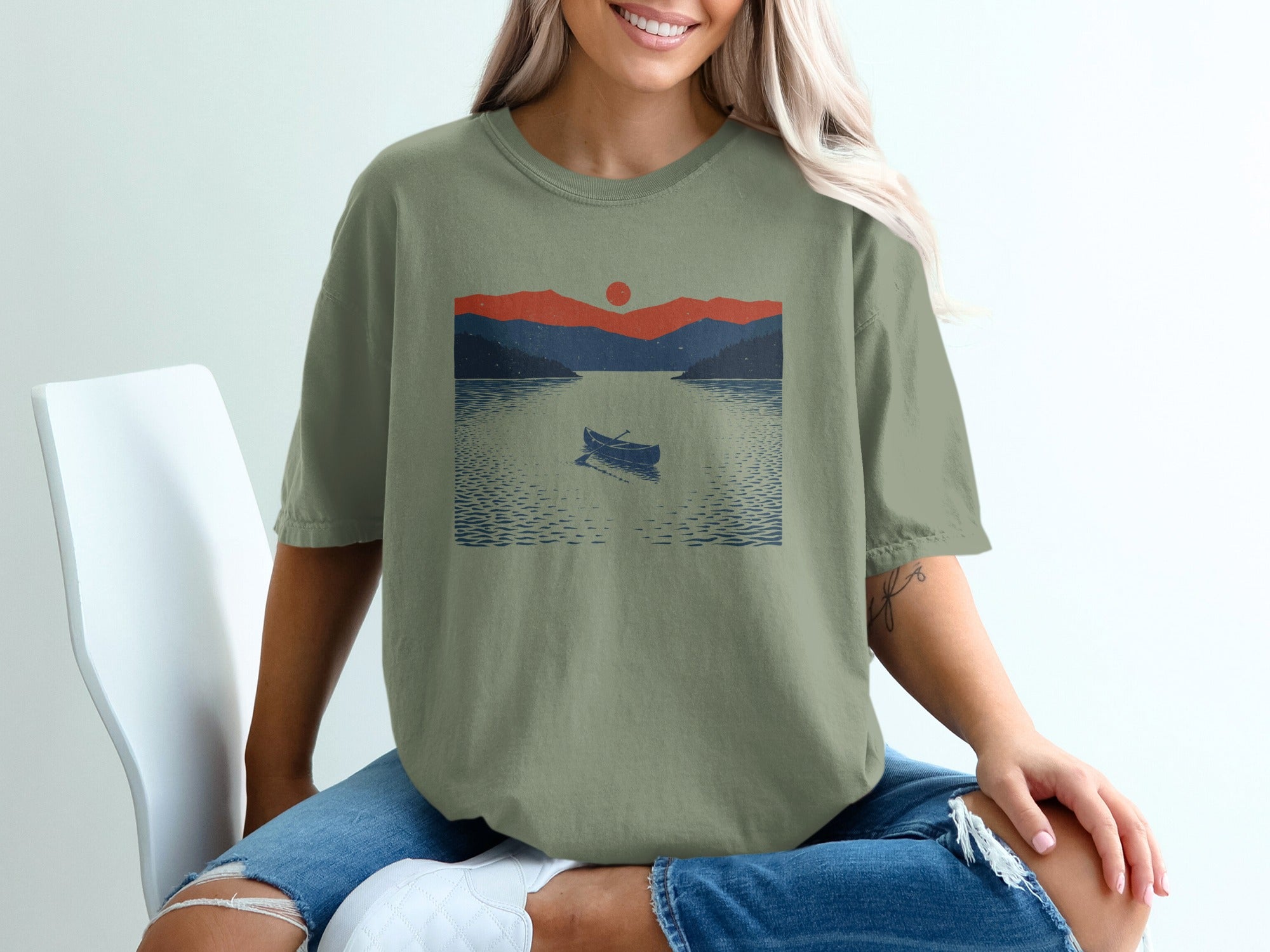Olive green t-shirt graphic with a canoe on a lake at sunset.