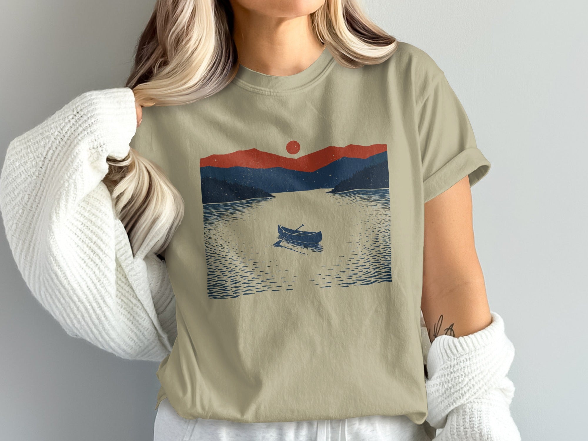 Tan t-shirt with a graphic of a lone canoe on a lake at sunset.