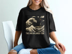 Black t-shirt with graphic of a large wave, small boats, and text "THE UNEXPLAINED TIDE".