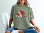 Running figure and bear silhouette against abstract geometric background on green t-shirt.
