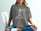Grey t-shirt with minimalist line art of a lighthouse on rocks and waves.