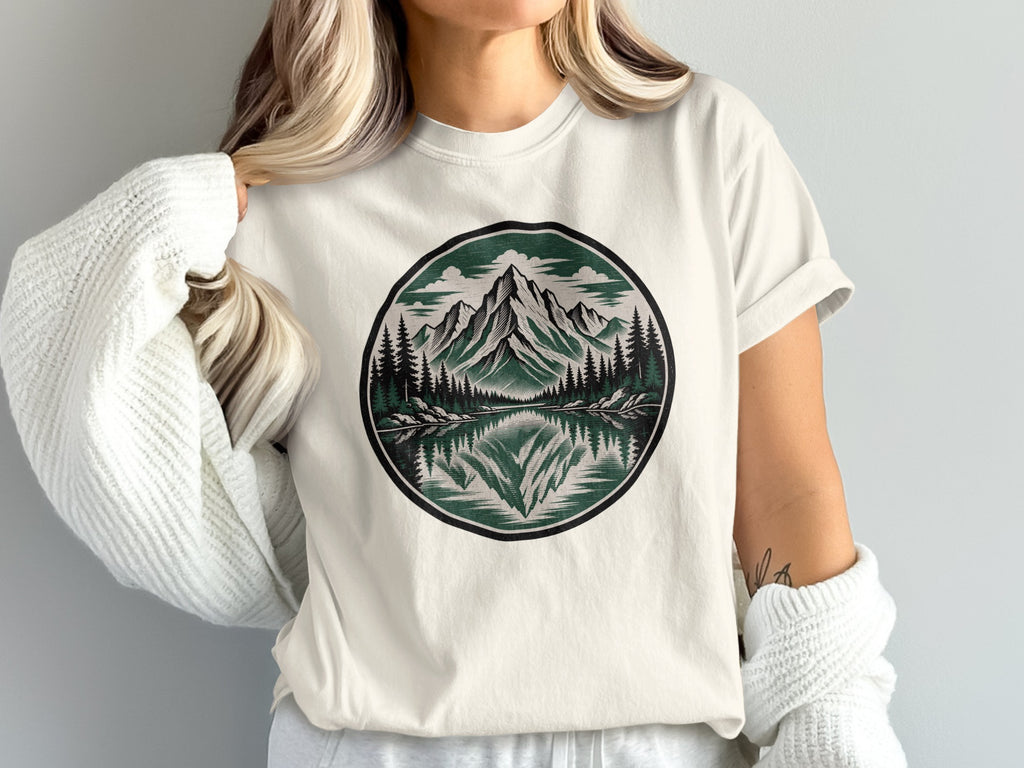 White t-shirt with circular mountain reflection graphic and forest detail.