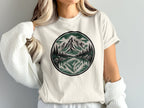 White t-shirt with circular mountain reflection graphic and forest detail.
