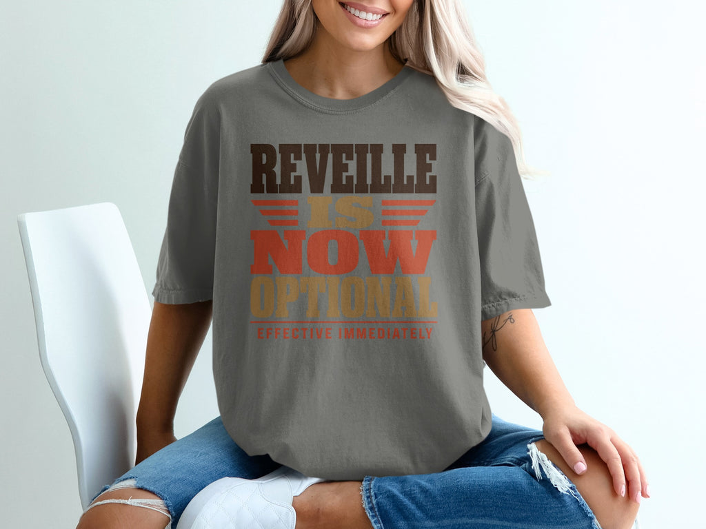 A person wears a gray t-shirt featuring the text REVEILLE IS NOW OPTIONAL EFFECTIVE IMMEDIATELY.