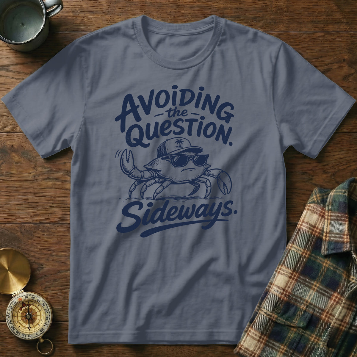 A slate blue t-shirt printed with a crab wearing sunglasses and a hat alongside the text avoiding the question sideways.