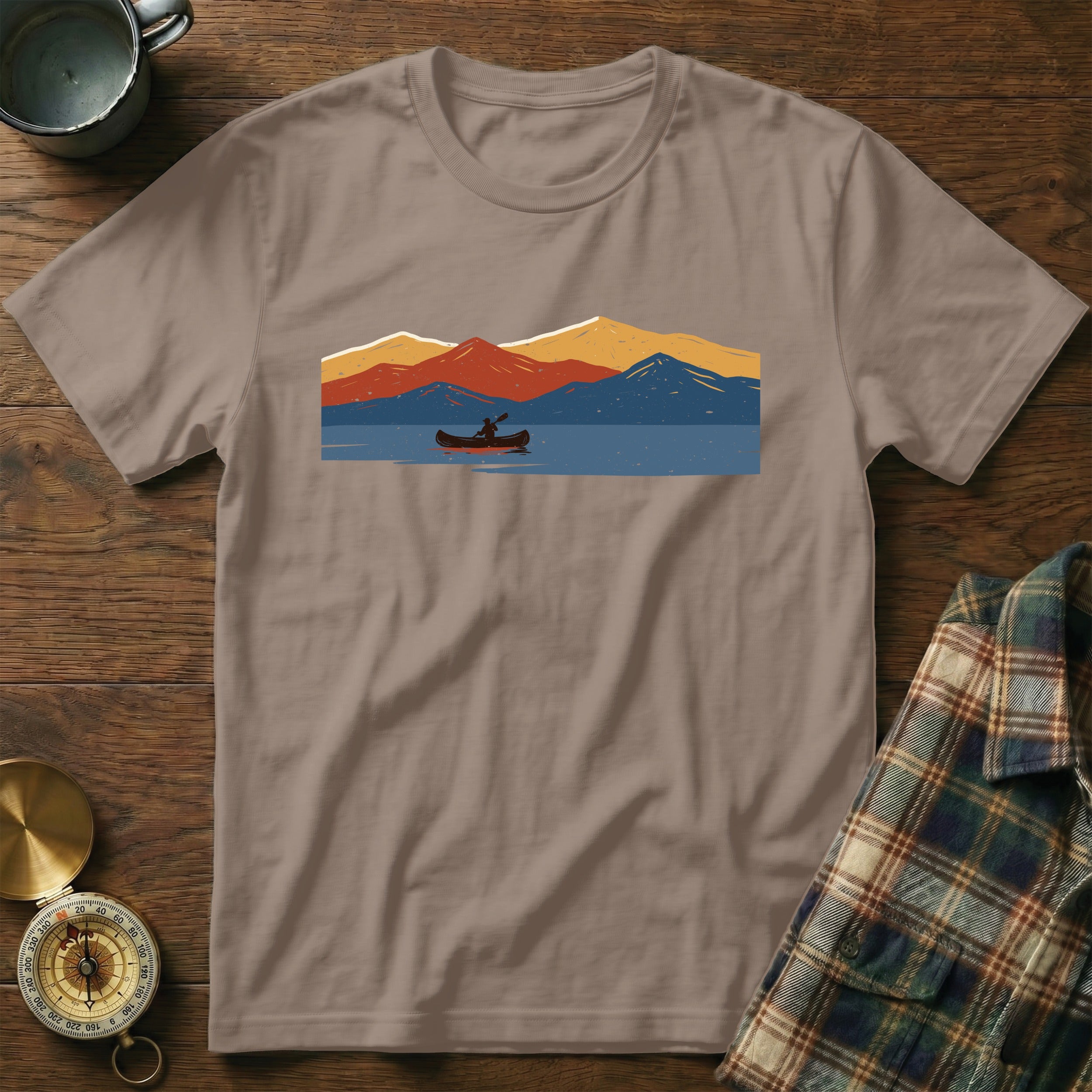 Brown t-shirt with a graphic of a canoeist on a lake with mountains.