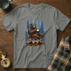 Bear sitting in a camping chair with a mug, forest background.