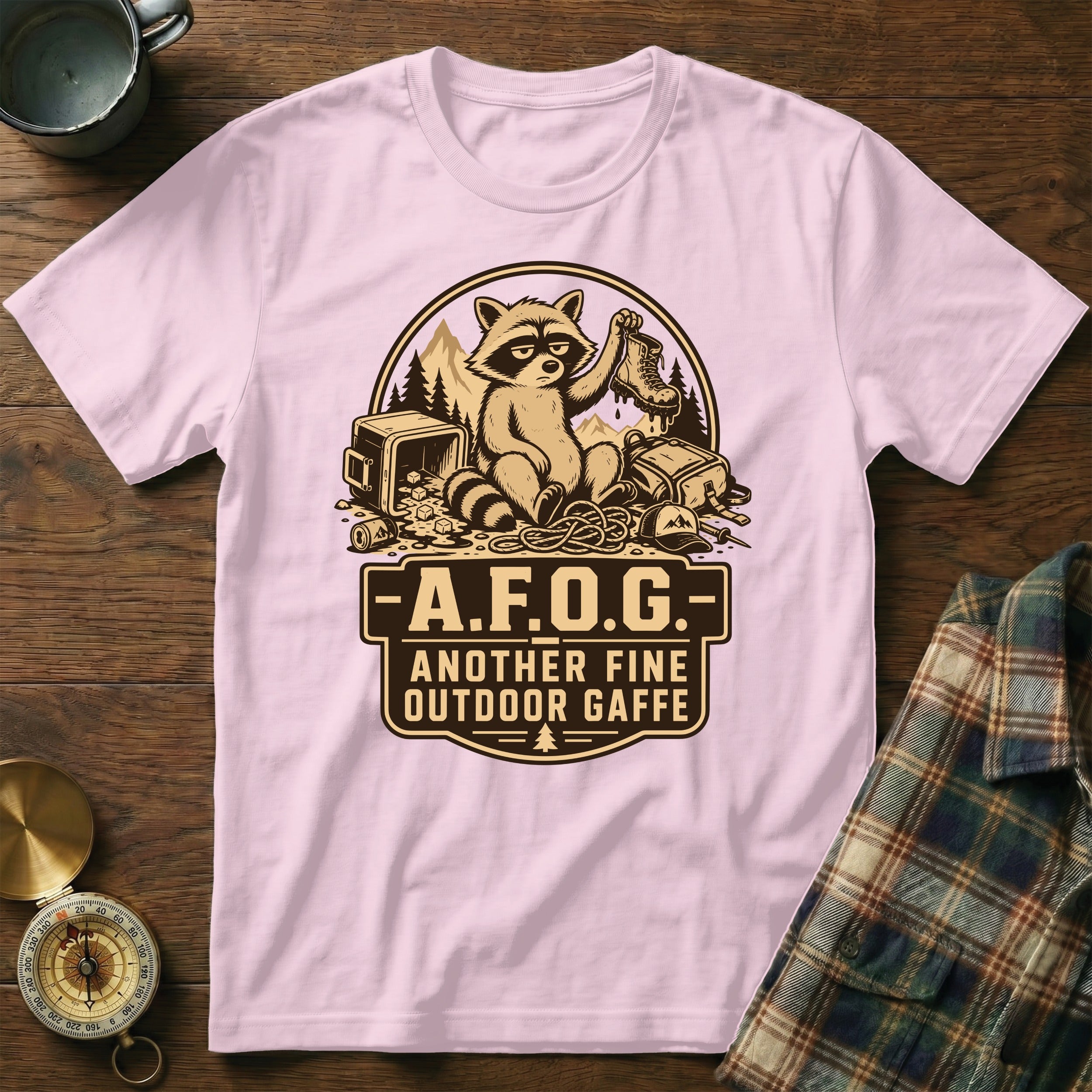 Light pink t-shirt with a graphic of a raccoon on camping gear and the text "A.F.O.G. Another Fine Outdoor Gaffe".