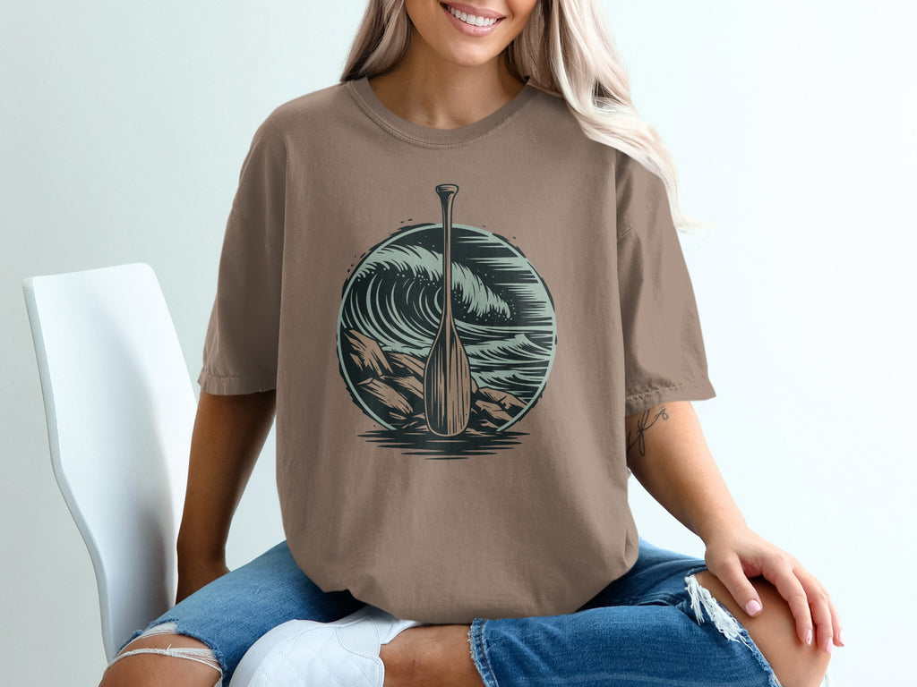 Round graphic with paddle and crashing wave on brown t-shirt.