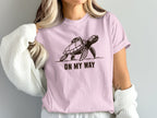 Pink t-shirt with a graphic of a turtle with a backpack and text "ON MY WAY".