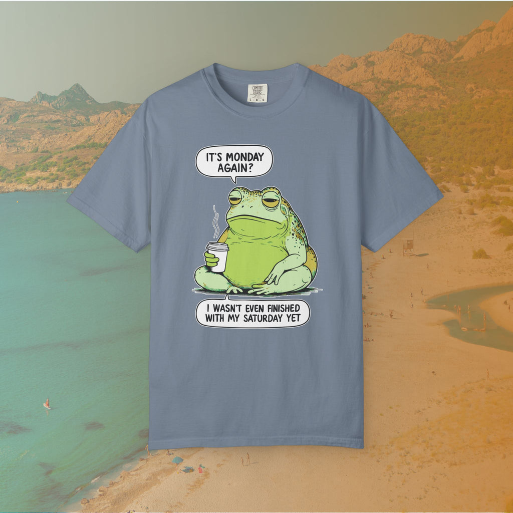 Blue T-shirt Funny T-shirt graphic featuring a large, grumpy toad holding a to-go coffee cup. The cartoon is captioned with the quotes: "IT'S MONDAY AGAIN? I WASN'T EVEN FINISHED WITH MY SATURDAY YET.