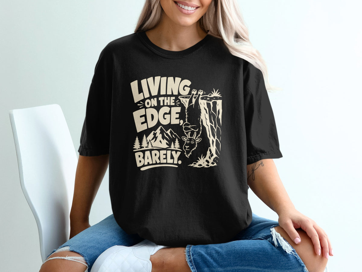 Black t-shirt with "Living on the Edge, Barely" text and a goat hanging from a cliff.