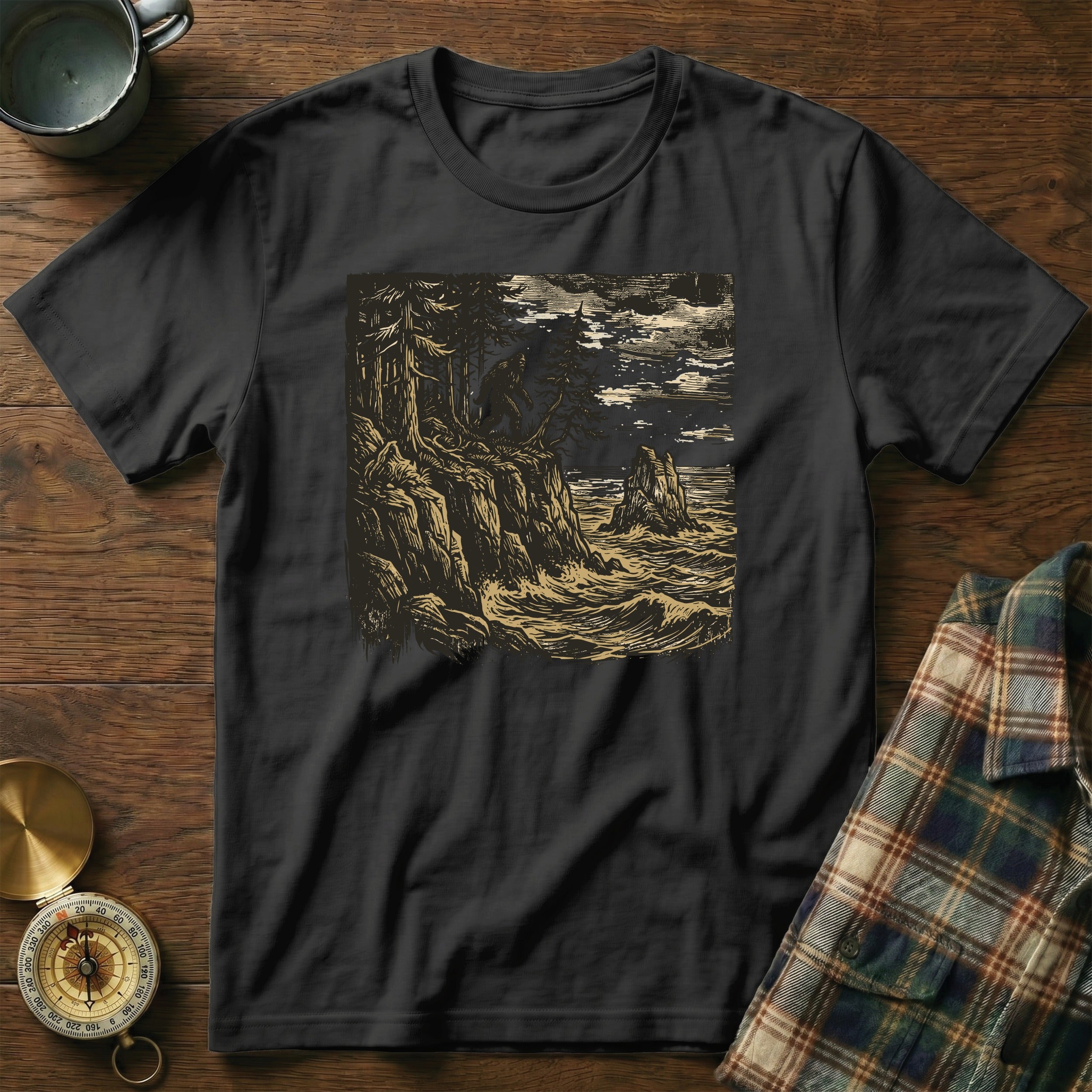 Dark t-shirt with a stylized woodland and ocean scene illustration.