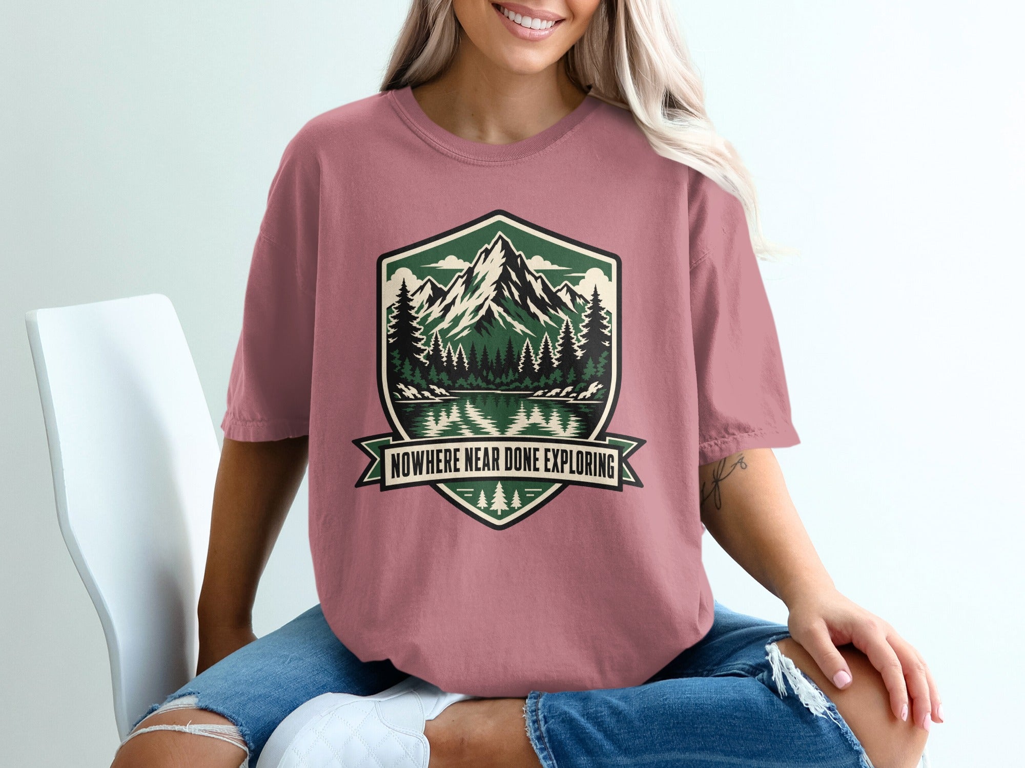 Pink t-shirt with mountain, forest, and lake graphic and text "NOWHERE NEAR DONE EXPLORING".