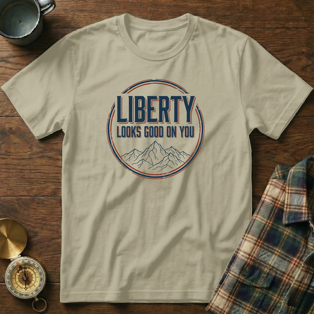 Sand t-shirt with "LIBERTY LOOKS GOOD ON YOU" graphic and mountain illustration.
