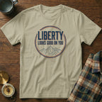 Sand t-shirt with "LIBERTY LOOKS GOOD ON YOU" graphic and mountain illustration.