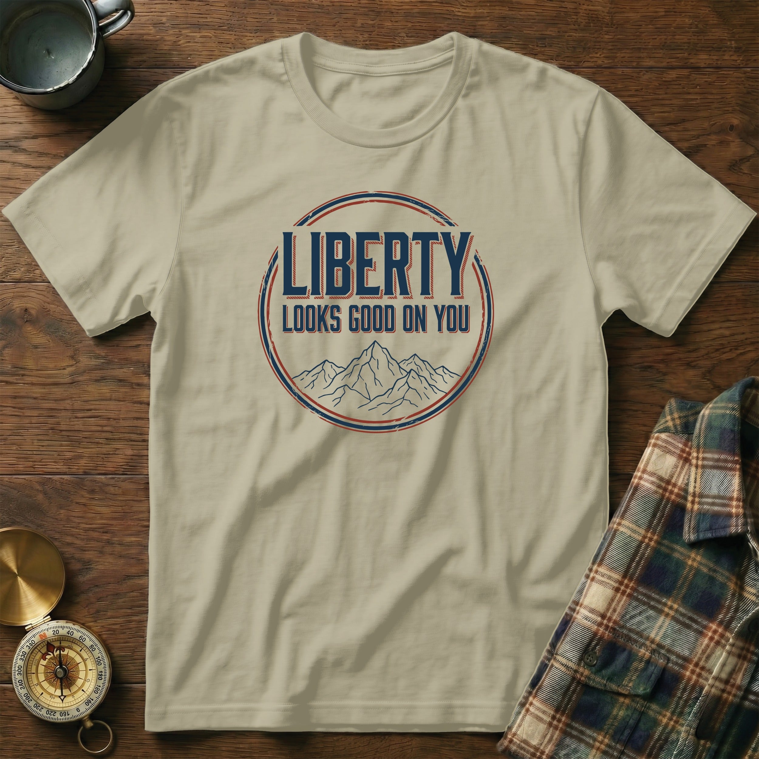 Sand t-shirt with "LIBERTY LOOKS GOOD ON YOU" graphic and mountain illustration.