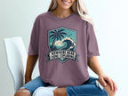 T-shirt with a crest graphic of a palm tree, ocean wave, and birds, text "Nowhere Near Done Exploring".