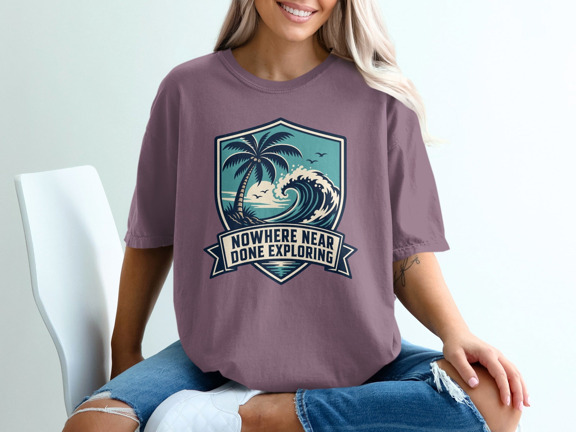 T-shirt with a crest graphic of a palm tree, ocean wave, and birds, text "Nowhere Near Done Exploring".