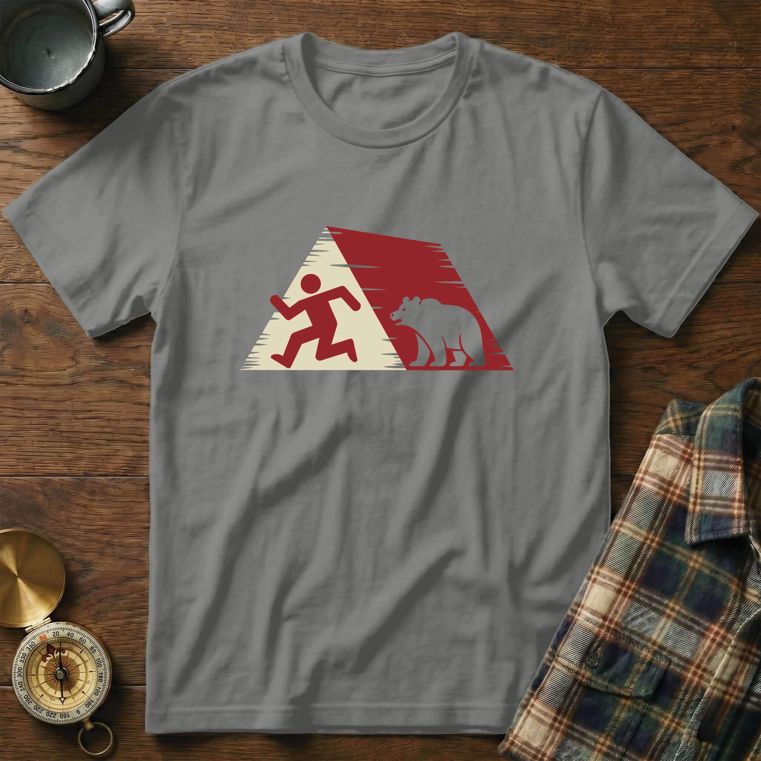 Gray t-shirt with running person and bear graphic, plaid shirt and compass nearby.