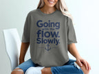 A woman wearing a grey t-shirt featuring navy blue text that reads Going with the flow. Slowly. and an anchor graphic.