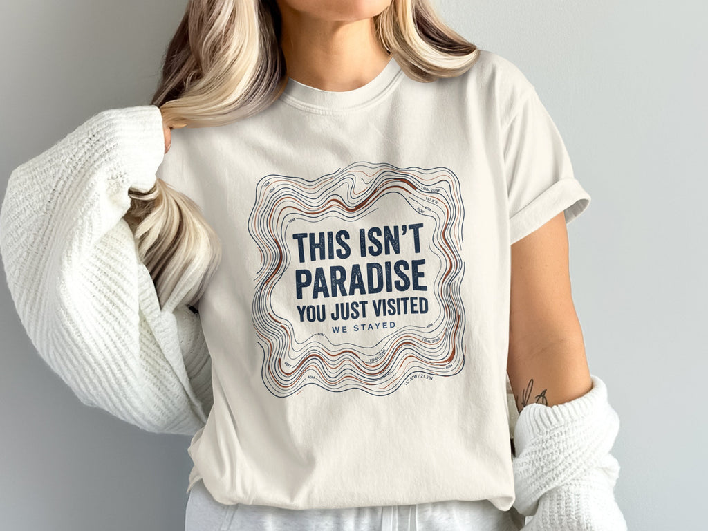 White t-shirt with "This Isn't Paradise You Just Visited We Stayed" text.