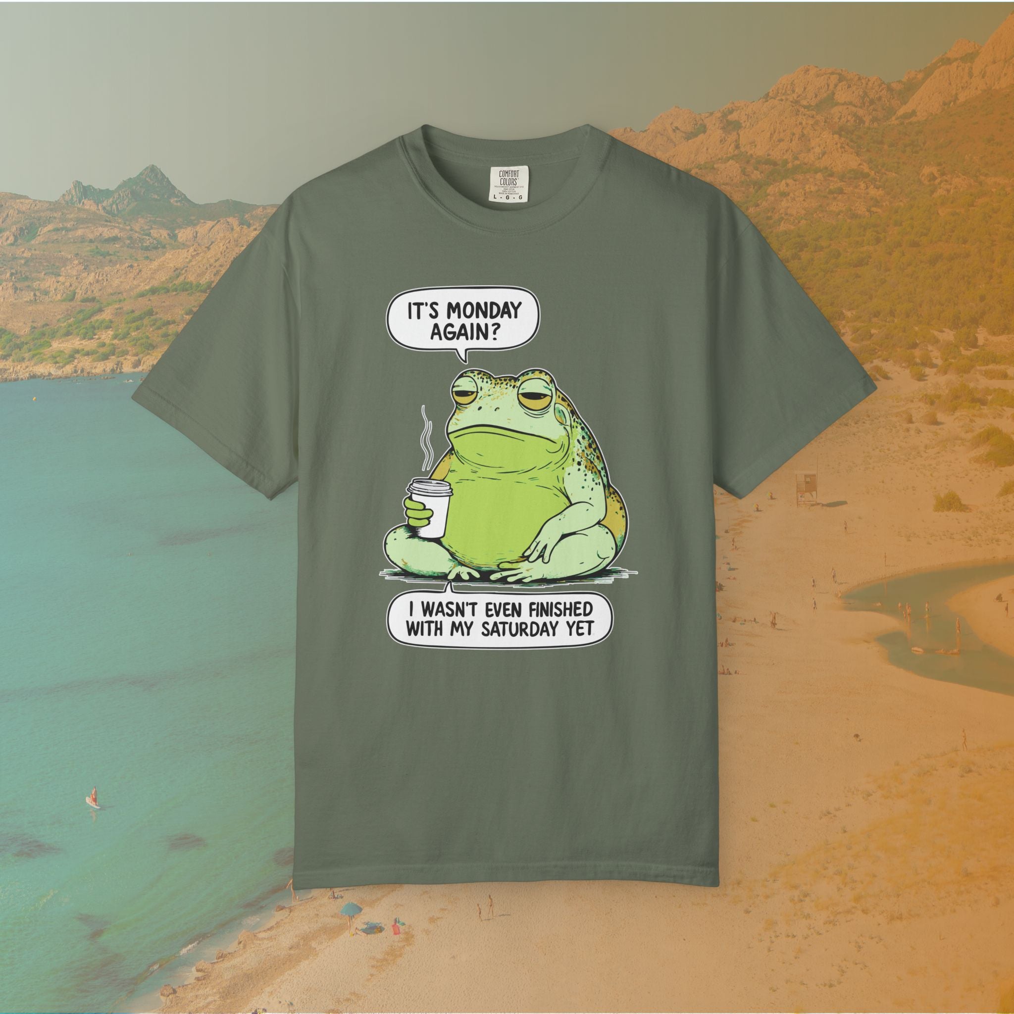 Green T-shirt Funny T-shirt graphic featuring a large, grumpy toad holding a to-go coffee cup. The cartoon is captioned with the quotes: "IT'S MONDAY AGAIN? I WASN'T EVEN FINISHED WITH MY SATURDAY YET.