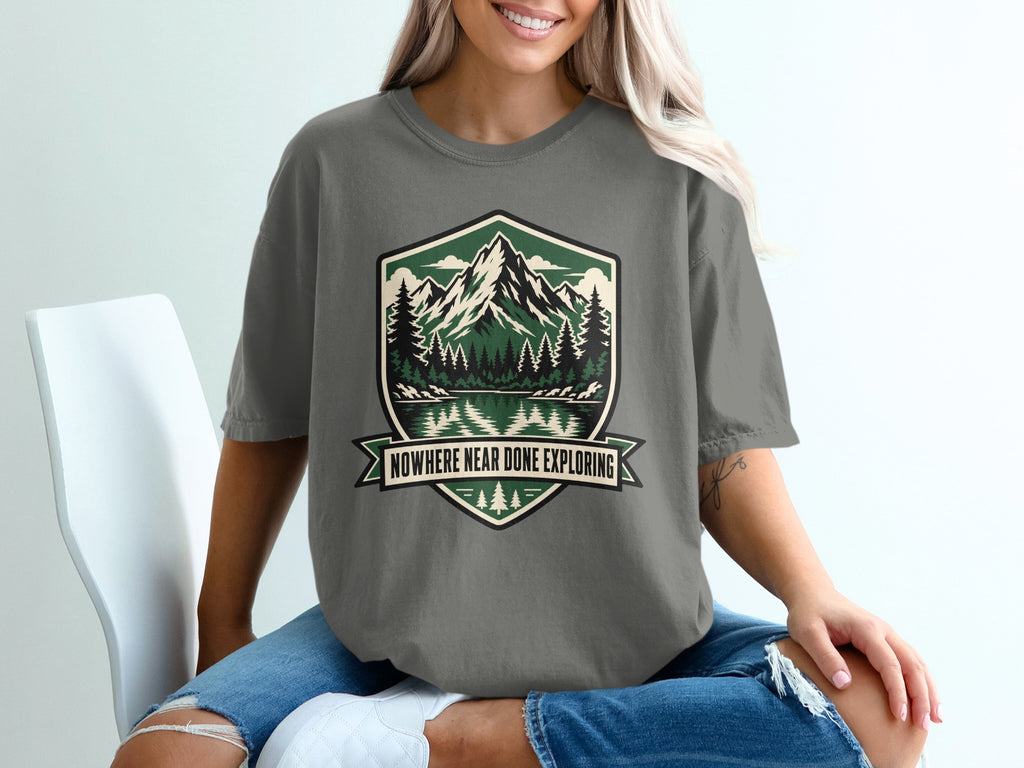 T-shirt with a shield graphic featuring mountains, trees, lake, and text "NOWHERE NEAR DONE EXPLORING".