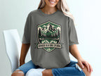 T-shirt with a shield graphic featuring mountains, trees, lake, and text "NOWHERE NEAR DONE EXPLORING".