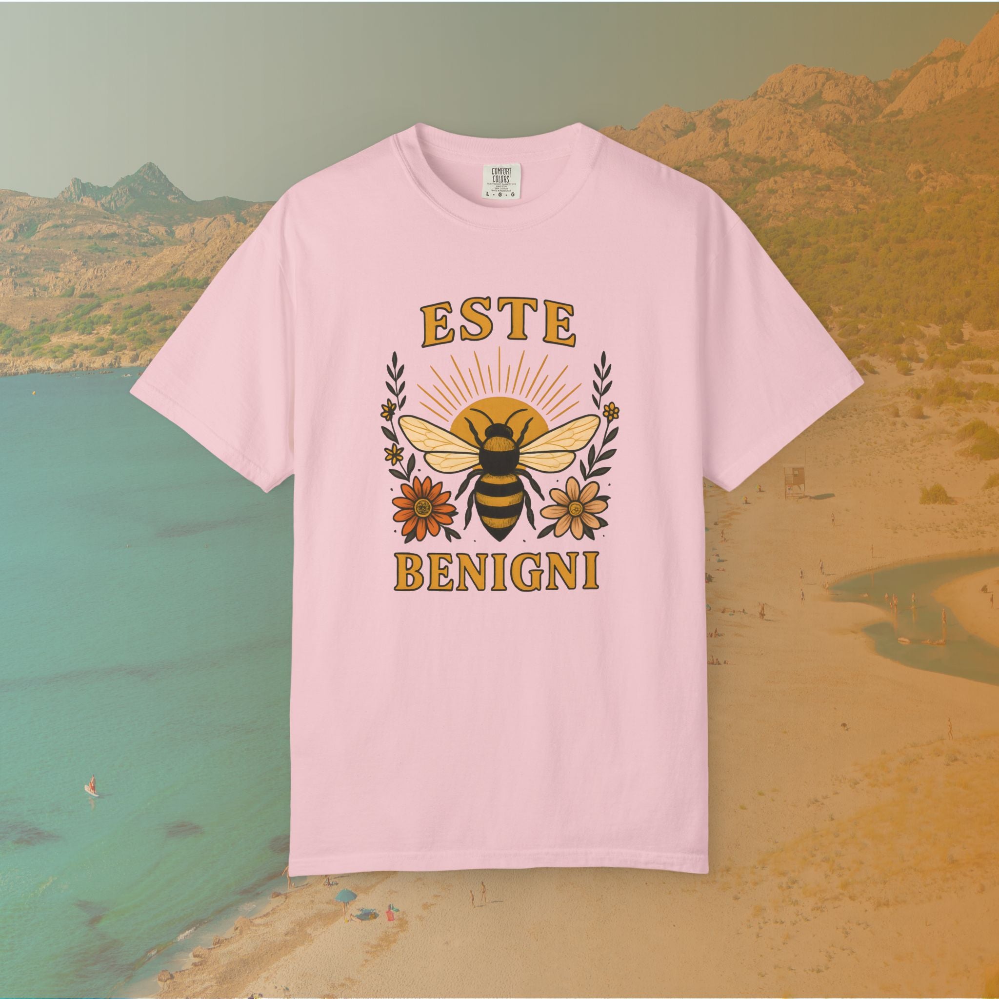 pink  t-shirt Vintage-style graphic tee featuring a large, central honey bee with sunburst wings, flanked by retro flowers. The Latin words "ESTE BENIGNI" for "BEE KIND" are printed above and below the design.