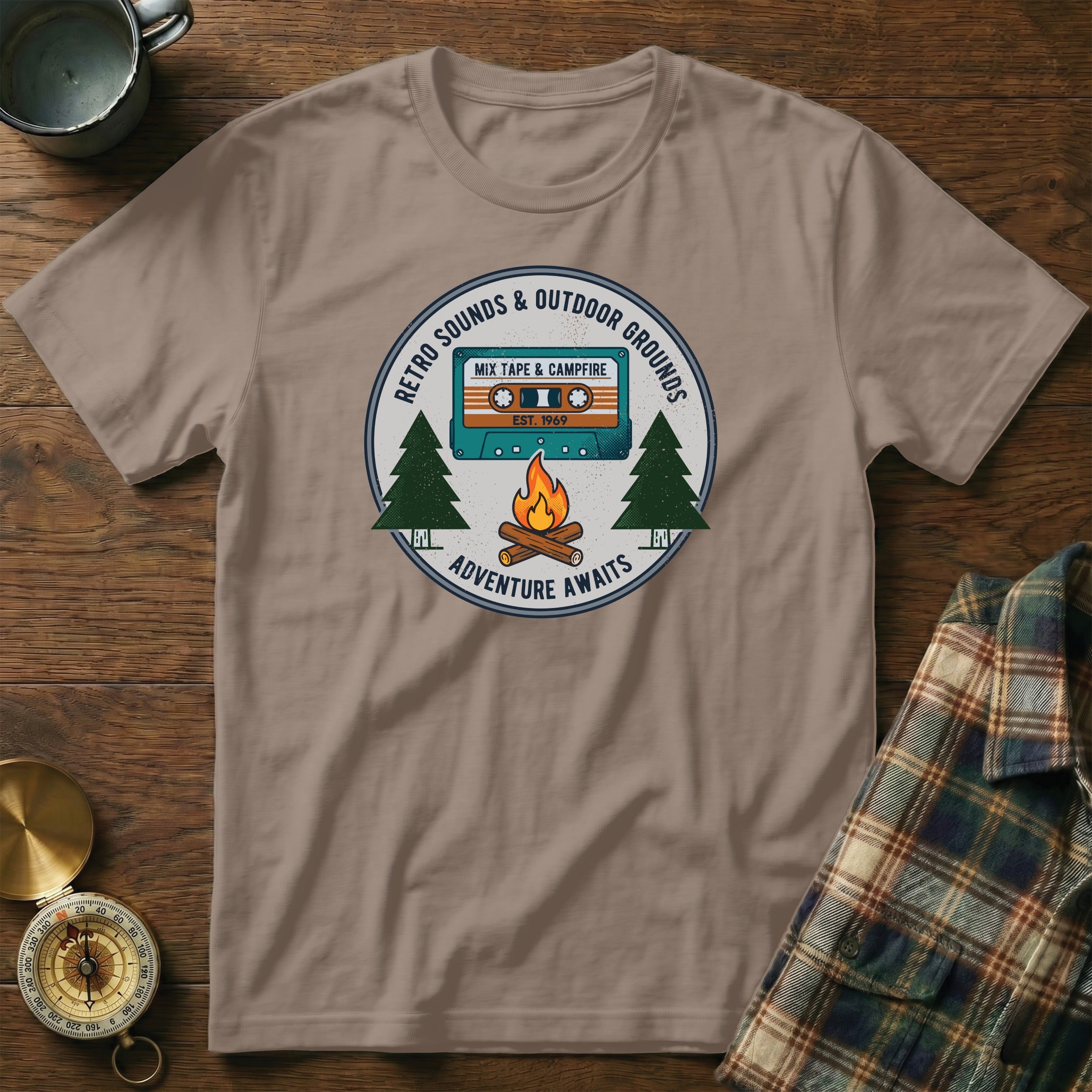T-shirt graphic: retro mixtape, campfire, trees, and "Adventure Awaits" text.