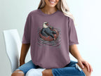 Eagle with sunglasses floats on inner tube with drink, printed on purple t-shirt.