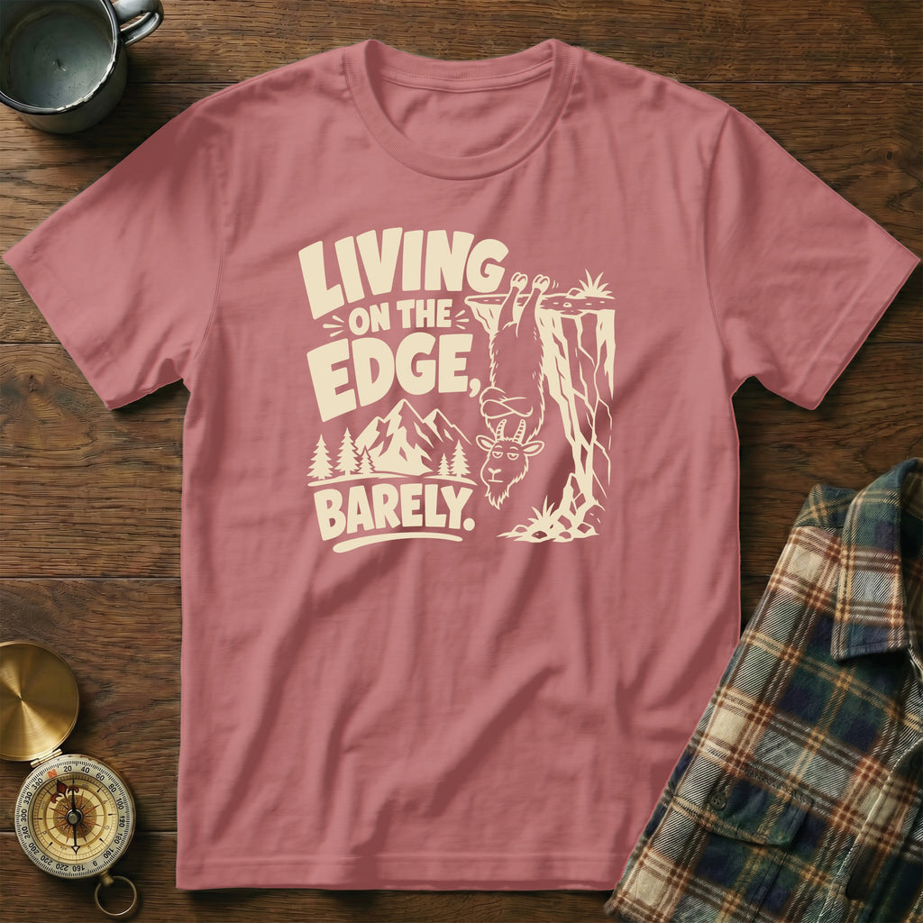 T-shirt with a goat hanging off a cliff, text "LIVING ON THE EDGE, BARELY."