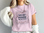 Pink t-shirt with topographic map design and text "THIS ISN'T PARADISE YOU JUST VISITED WE STAYED".