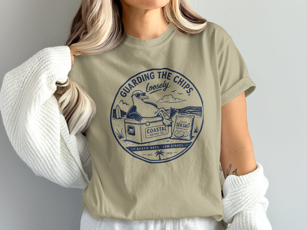 Tan t-shirt with "Guarding the Chips Loosely" text and beach scene graphic.