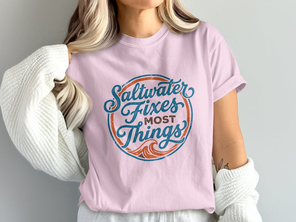Pink t-shirt with blue and orange circular graphic that reads "Saltwater Fixes Most Things".