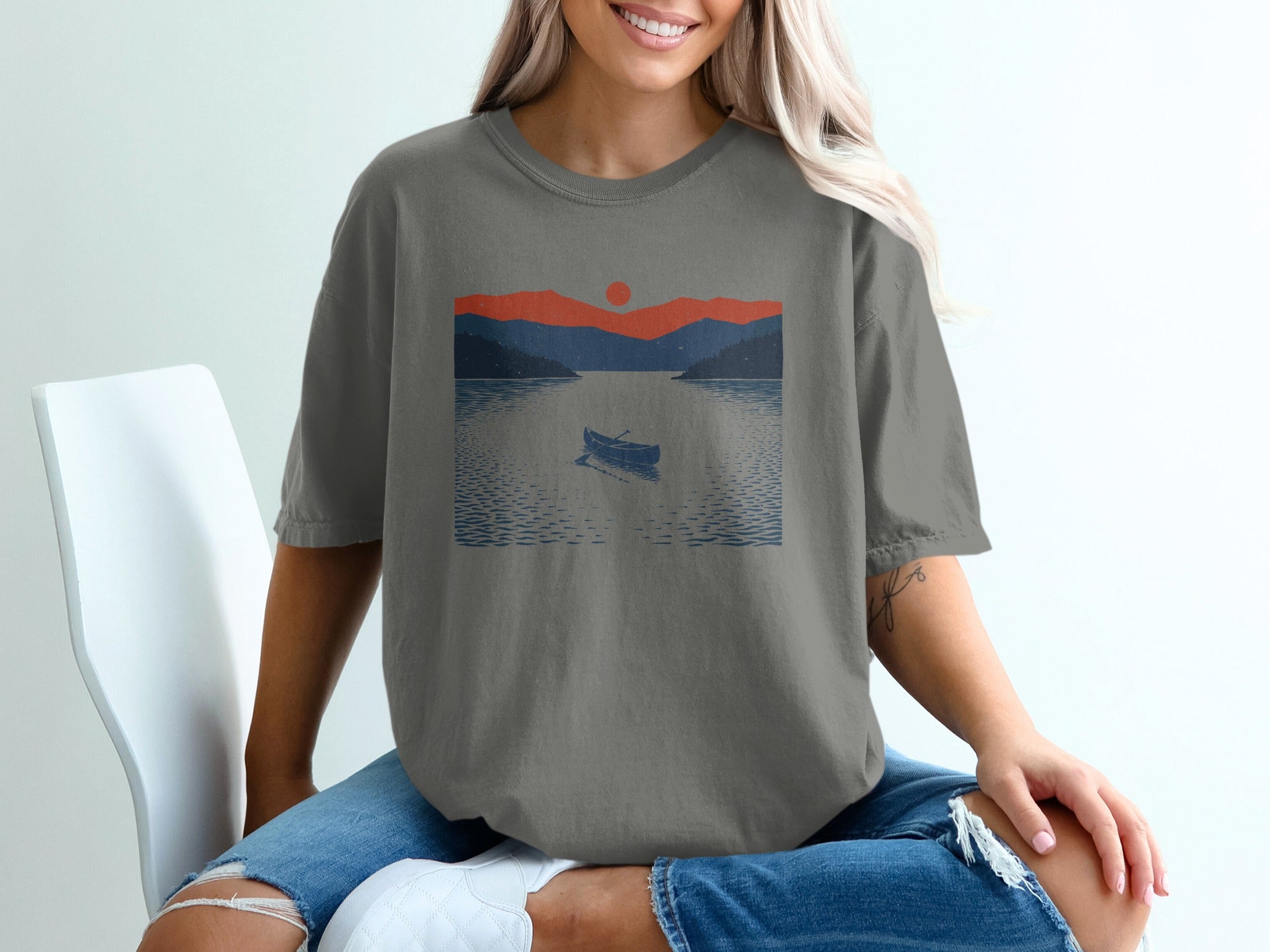 Graphic on t-shirt shows a canoe on a lake with mountains and sunset.