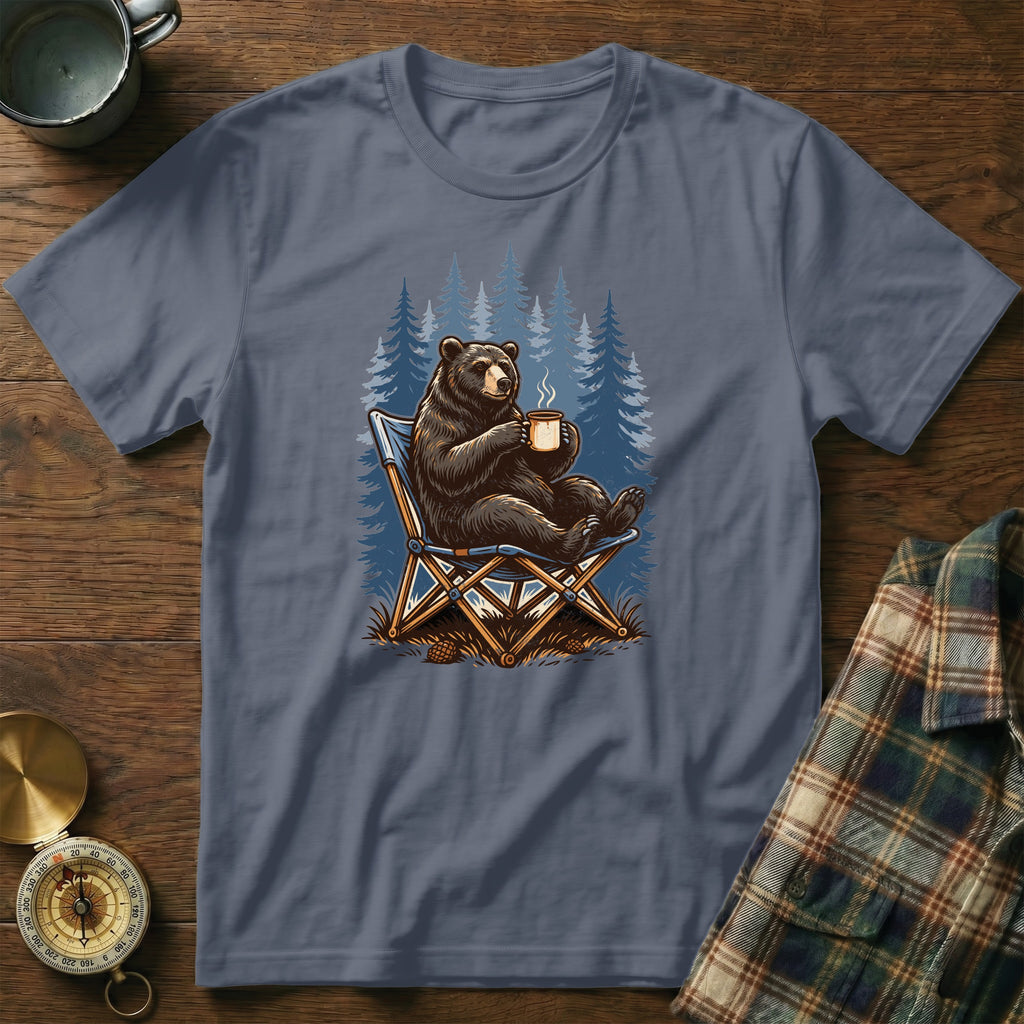 Bear sitting in a chair holding a coffee mug with trees in the background.