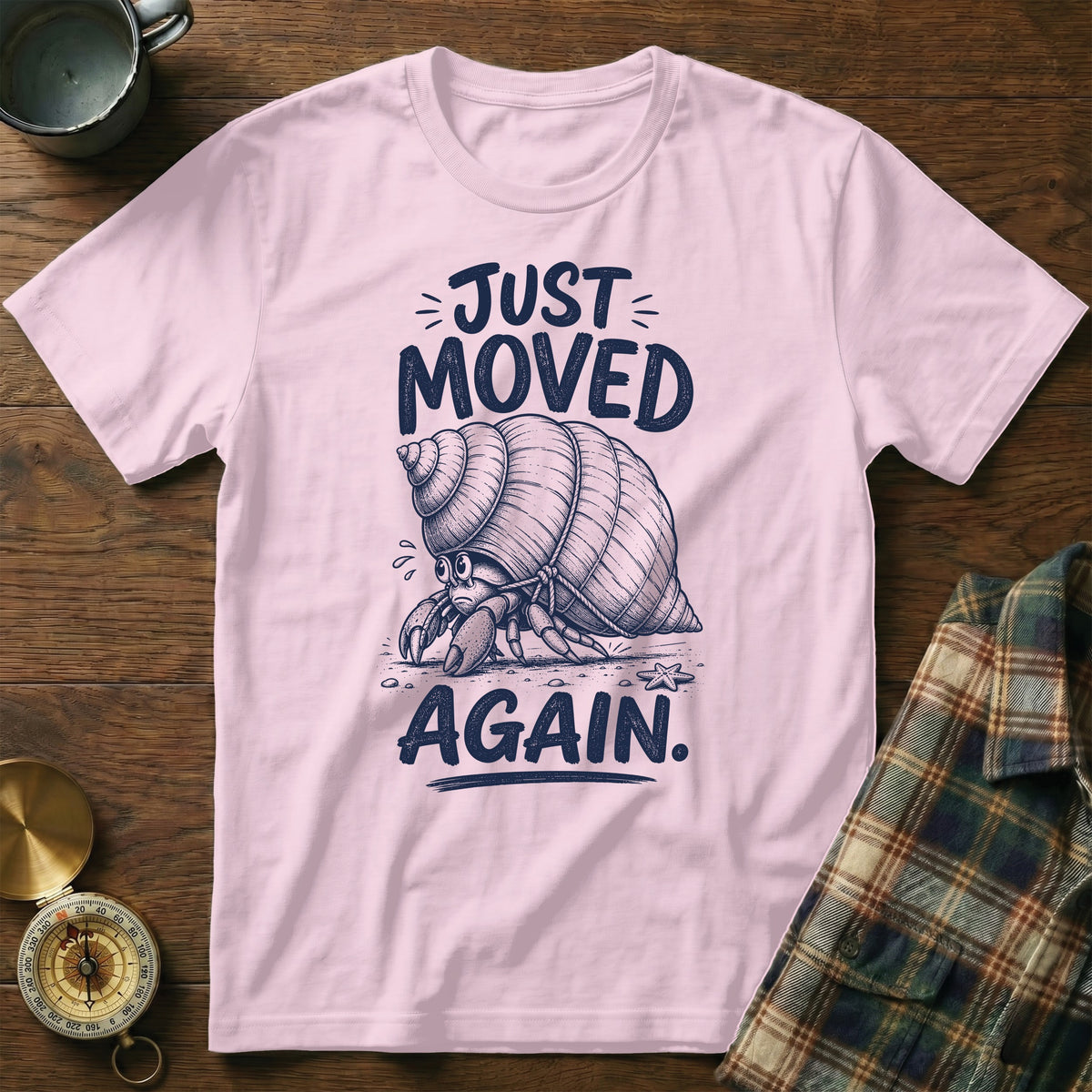 Pink t-shirt with a sketch of a sad hermit crab and text "JUST MOVED AGAIN."
