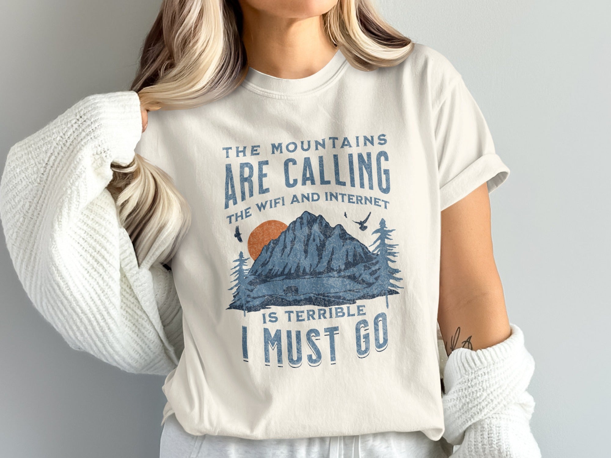 Cream t-shirt with "The mountains are calling, the wifi and internet is terrible, I must go" text and mountain graphic.