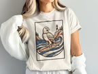 T-shirt with graphic of an eagle surfing by a lighthouse during the day.