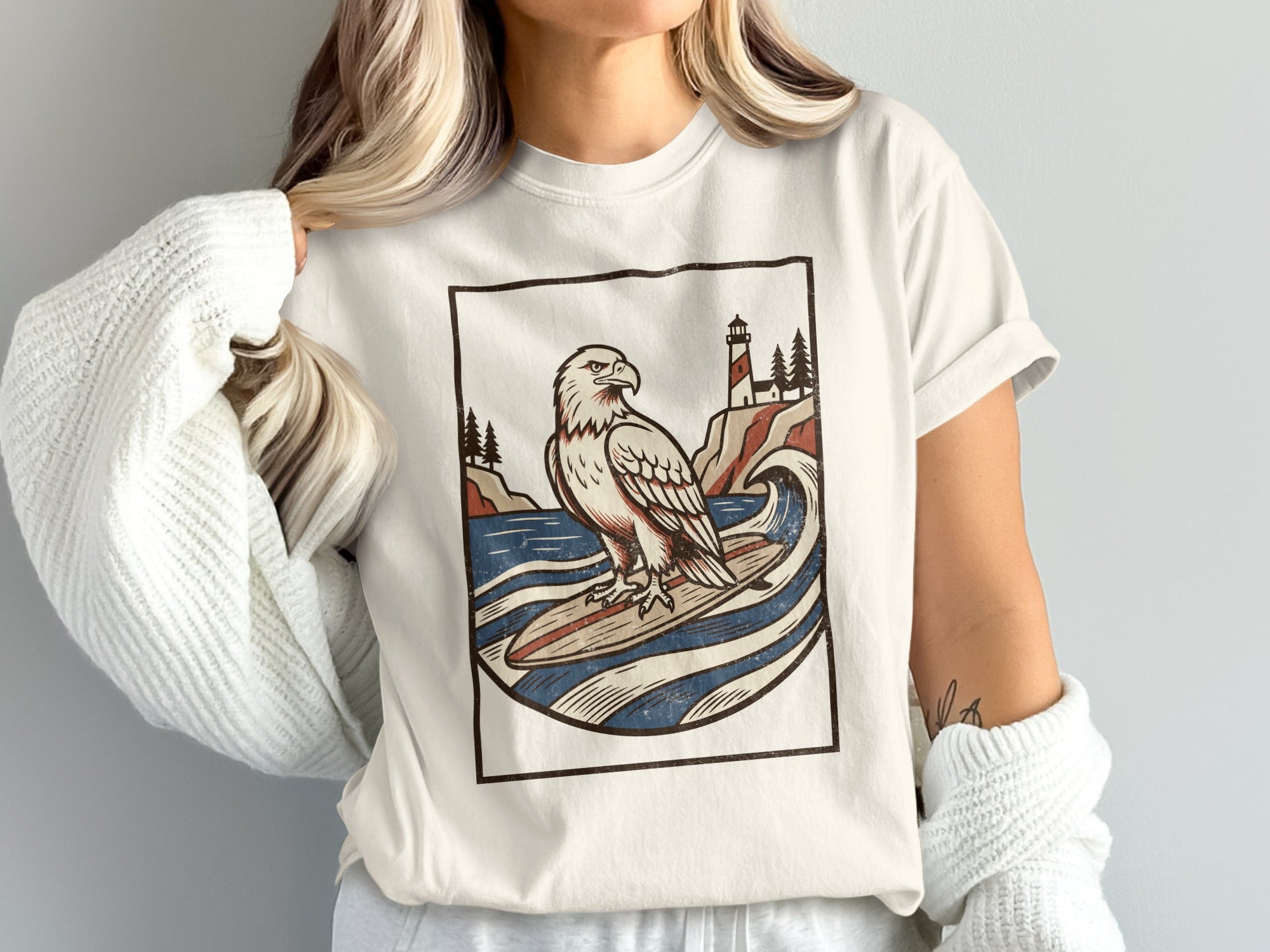 T-shirt with graphic of an eagle surfing by a lighthouse during the day.