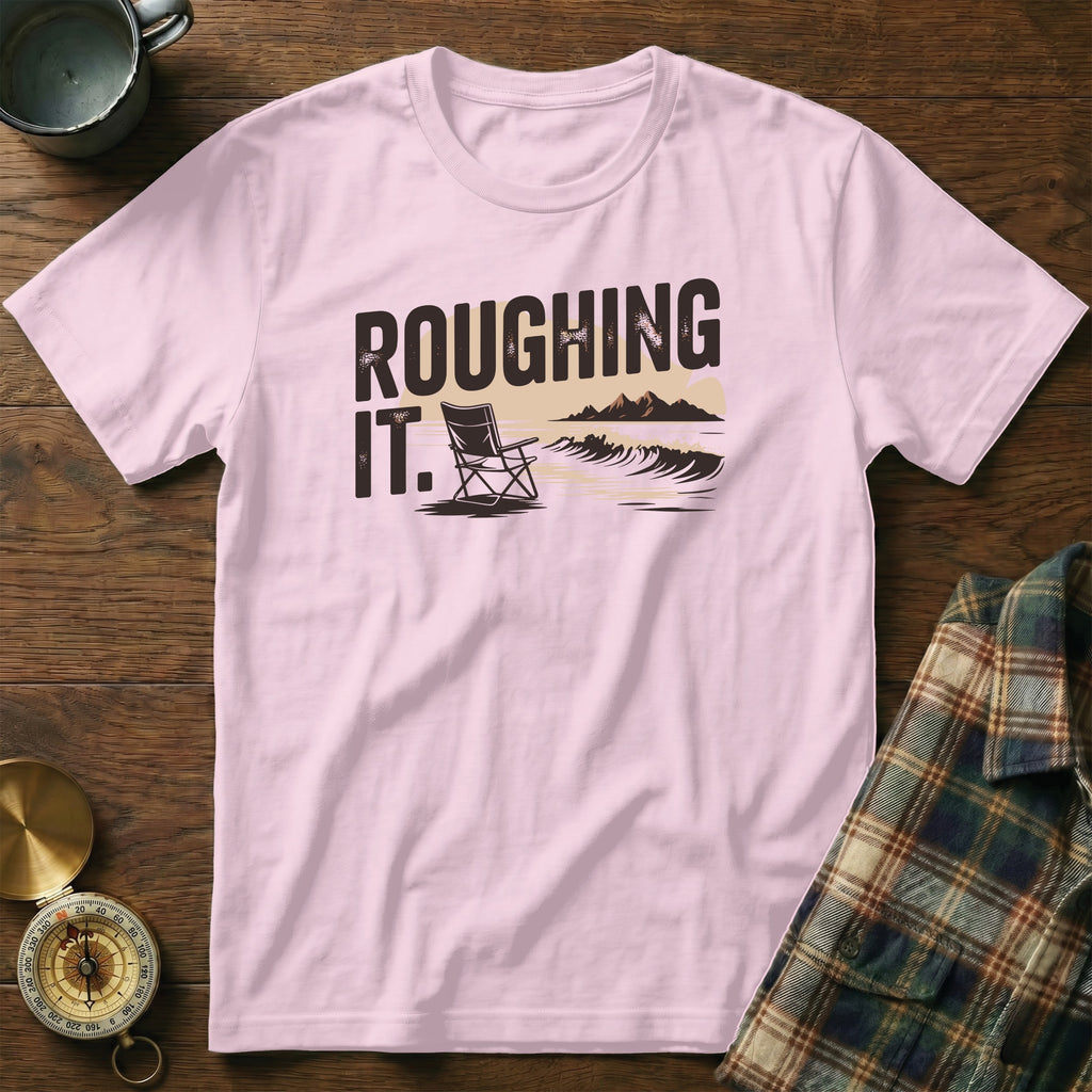 Pink t-shirt with "ROUGHING IT." text and a camp chair by the ocean.